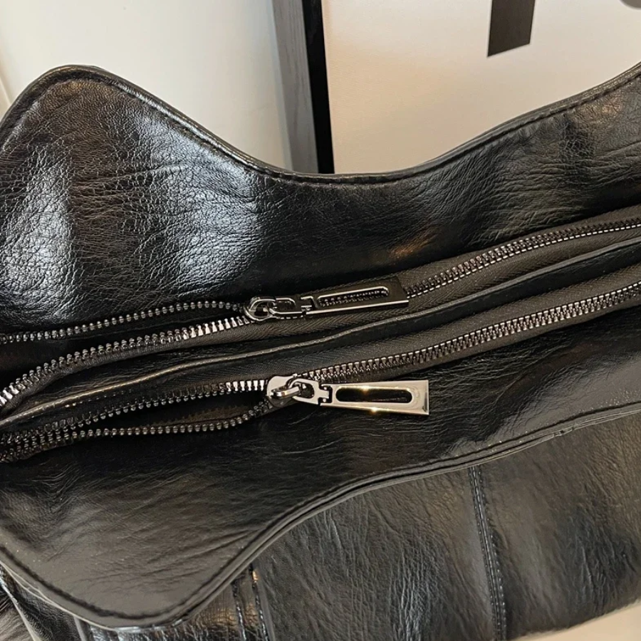 "Amber schoudertas van zacht, vegan leer met elegante metalen details. Ruime, georganiseerde indeling voor dagelijks gebruik.