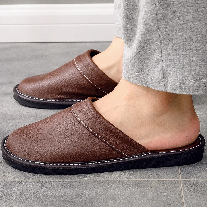 "Heren leren pantoffels met zachte voering, ergonomisch ontwerp en duurzame zool in zwart, getoond op een houten vloer."