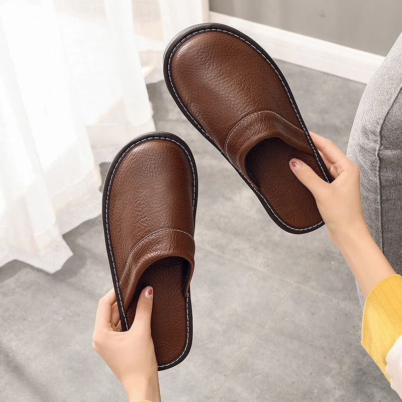"Heren leren pantoffels met zachte voering, ergonomisch ontwerp en duurzame zool in zwart, getoond op een houten vloer."