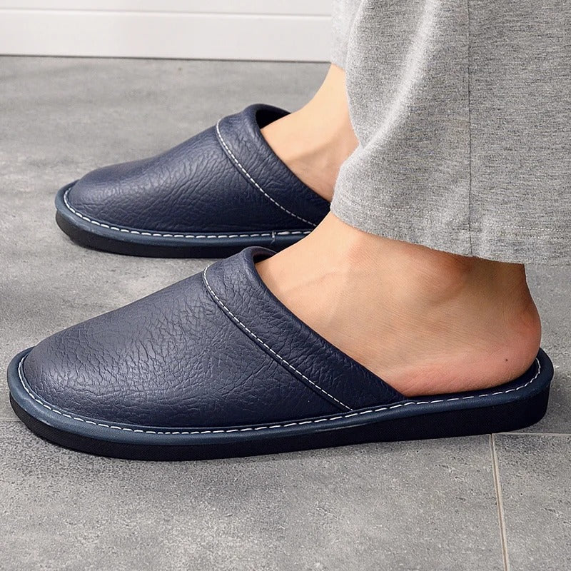 "Heren leren pantoffels met zachte voering, ergonomisch ontwerp en duurzame zool in zwart, getoond op een houten vloer."