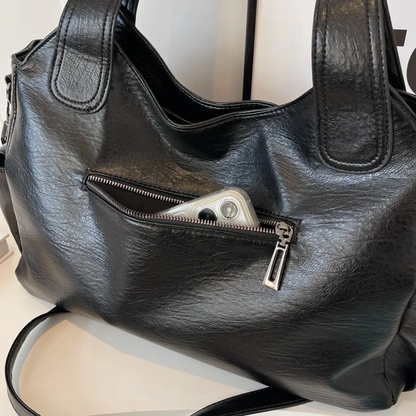 "Amber schoudertas van zacht, vegan leer met elegante metalen details. Ruime, georganiseerde indeling voor dagelijks gebruik.