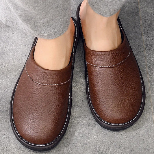 "Heren leren pantoffels met zachte voering, ergonomisch ontwerp en duurzame zool in zwart, getoond op een houten vloer."