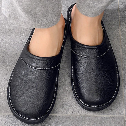 "Heren leren pantoffels met zachte voering, ergonomisch ontwerp en duurzame zool in zwart, getoond op een houten vloer."